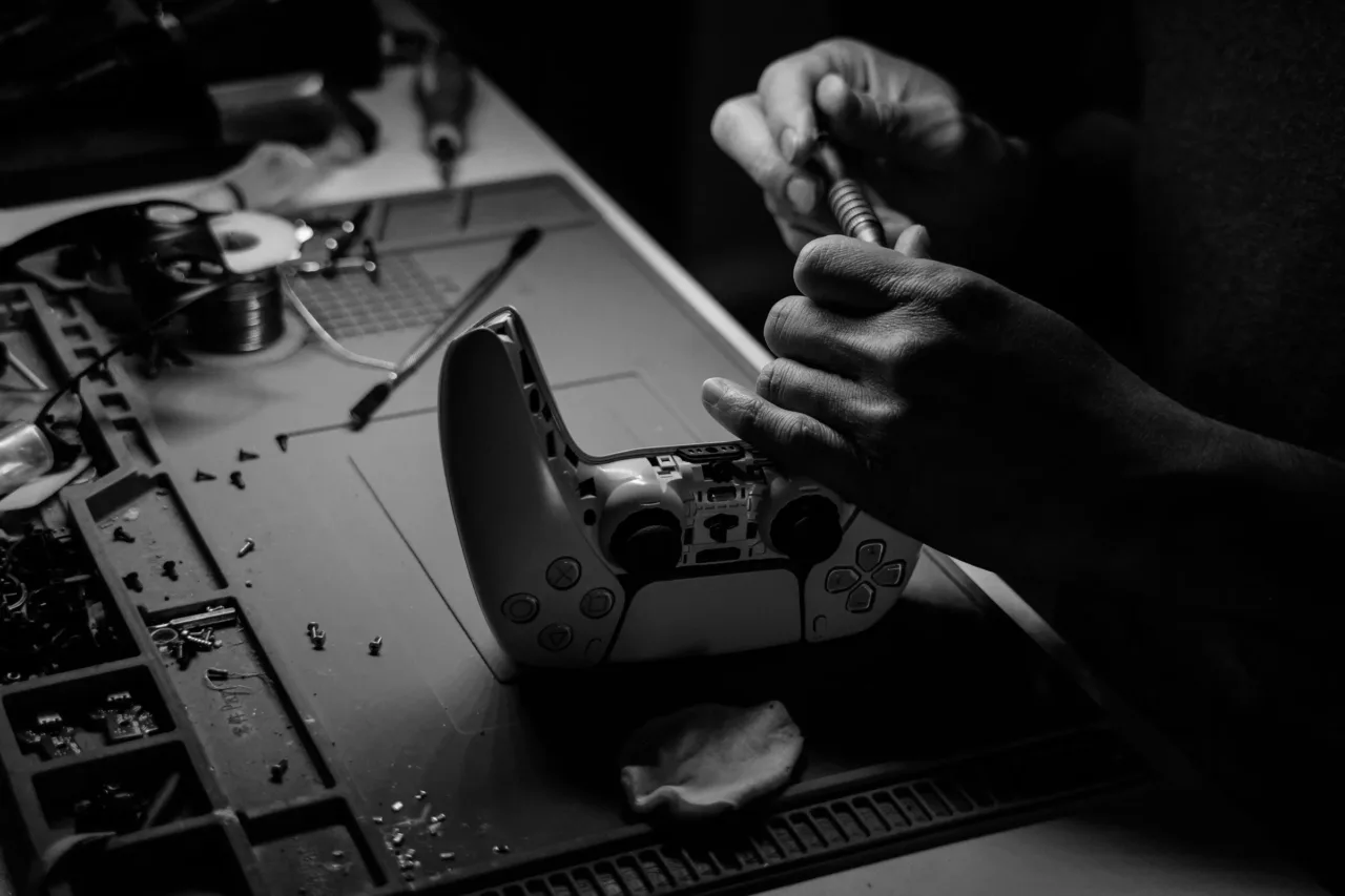 Hände reparieren einen geöffneten PlayStation-Controller auf der Werkbank