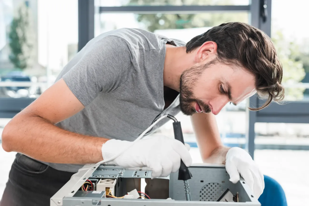 Techniker mit Schutzhandschuhen schraubt an einem geöffneten Computer